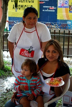 A mother works at a street grill with her little girl on her lap